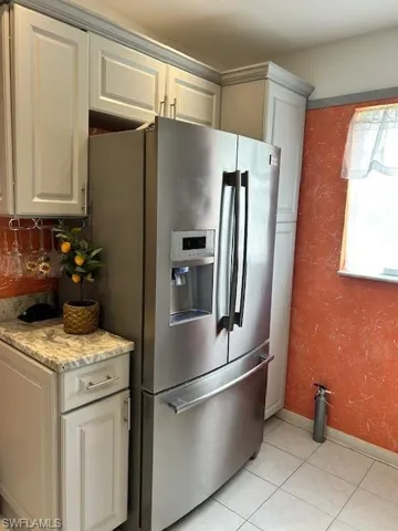 Kitchen featuring stainless steel fridge, light tile patterned floors, light stone countertops, and a textured wall