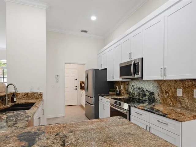 Kitchen with stainless steel appliances, dark stone countertops, ornamental molding, sink, and white cabinets