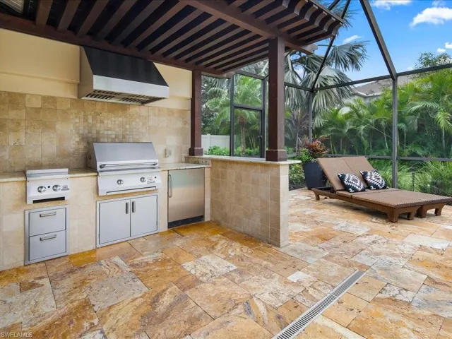 View of patio featuring exterior kitchen, glass enclosure, and a grill