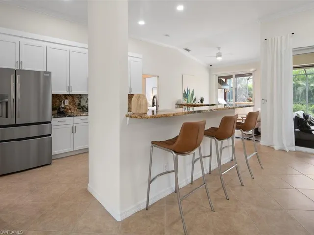 Kitchen with a kitchen bar, kitchen peninsula, stainless steel fridge, white cabinets, and light stone counters