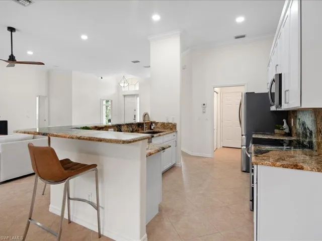 Kitchen with stone countertops, ornamental molding, sink, range, and white cabinetry