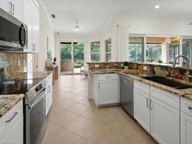 Kitchen with white cabinetry, stone counters, appliances with stainless steel finishes, and sink