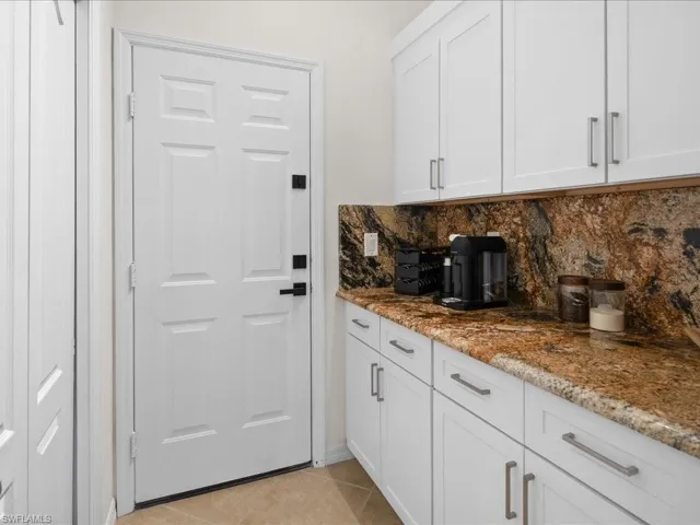 Kitchen featuring light tile patterned flooring, decorative backsplash, white cabinets, and light stone counters