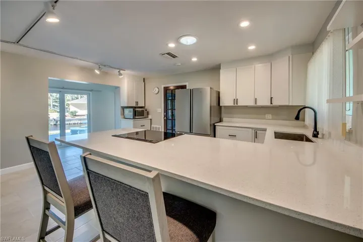 Kitchen with sink, kitchen peninsula, stainless steel fridge, black electric cooktop, and white cabinets
