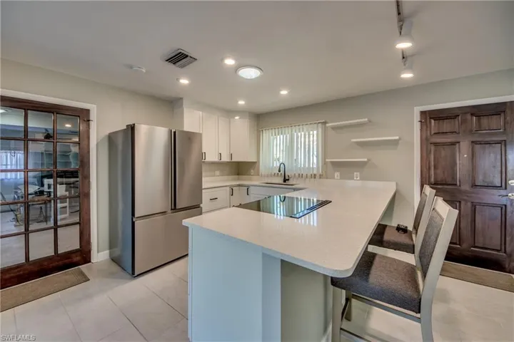 Kitchen with stainless steel refrigerator, white cabinetry, sink, kitchen peninsula, and a breakfast bar