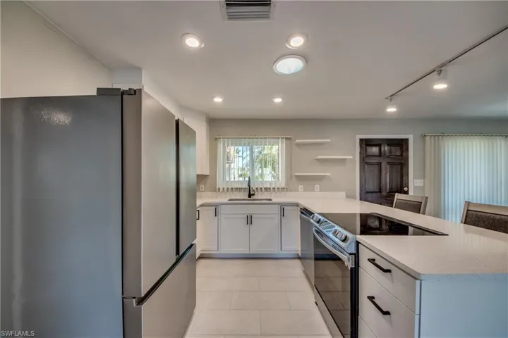 Kitchen with white cabinets, sink, light tile patterned flooring, light stone counters, and stainless steel appliances