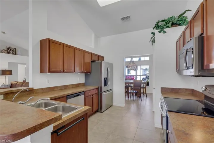 Kitchen featuring stainless steel appliances, wood finish cabinetry, a peninsula, vaulted ceiling, and light tile patterned flooring