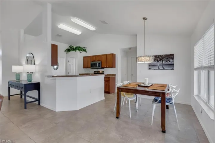 Kitchen with wood finish cabinetry, vaulted ceiling, decorative light fixtures, stainless steel microwave, and dark countertops