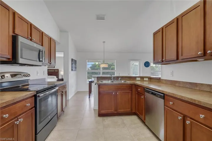 Kitchen featuring stainless steel appliances, wood finish cabinets, pendant lighting, a peninsula, and light tile patterned flooring