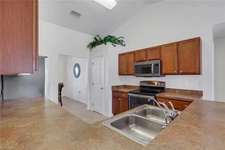 Kitchen featuring stainless steel appliances, wood finish cabinetry, light countertops, and lofted ceiling