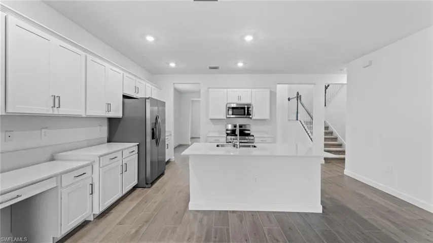 Kitchen with a kitchen island with sink, stainless steel appliances, light hardwood / wood-style floors, and white cabinetry