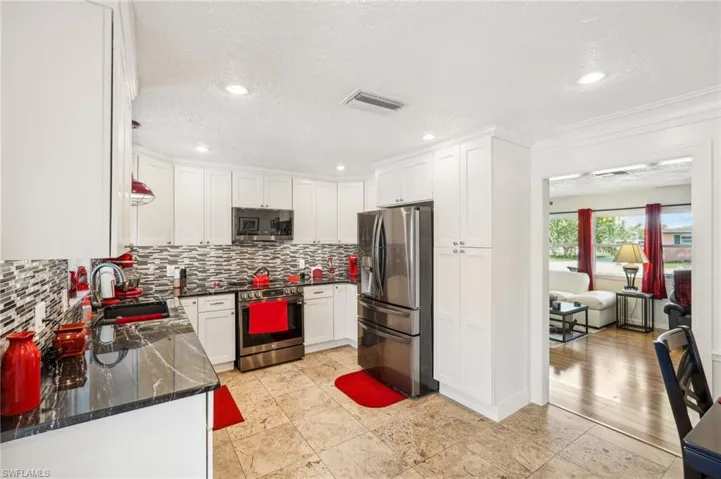 Kitchen with stainless steel appliances, granite counters, white cabinets, and decorative backsplash