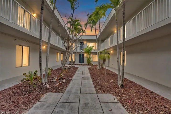 Courtyard entrance featuring a central paver pathway, mature palm trees, and landscaped beds with red mulch