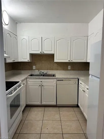 Kitchen featuring white cabinetry, light-toned countertops, a mosaic tile backsplash, stainless steel sink, and tile flooring