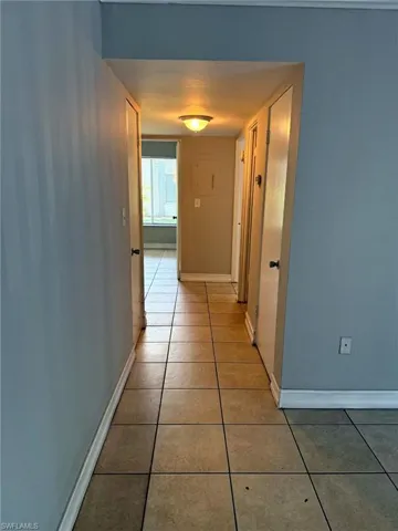 Hallway featuring square tile flooring, light blue wall paint, white baseboards, and a flush-mount ceiling light fixture
