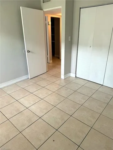 Light-colored tile flooring throughout, featuring a neutral wall color, white baseboards, and a white bi-fold closet door