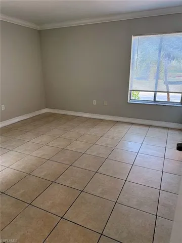 Spacious interior room featuring ceramic tile flooring, neutral wall paint, and white crown molding