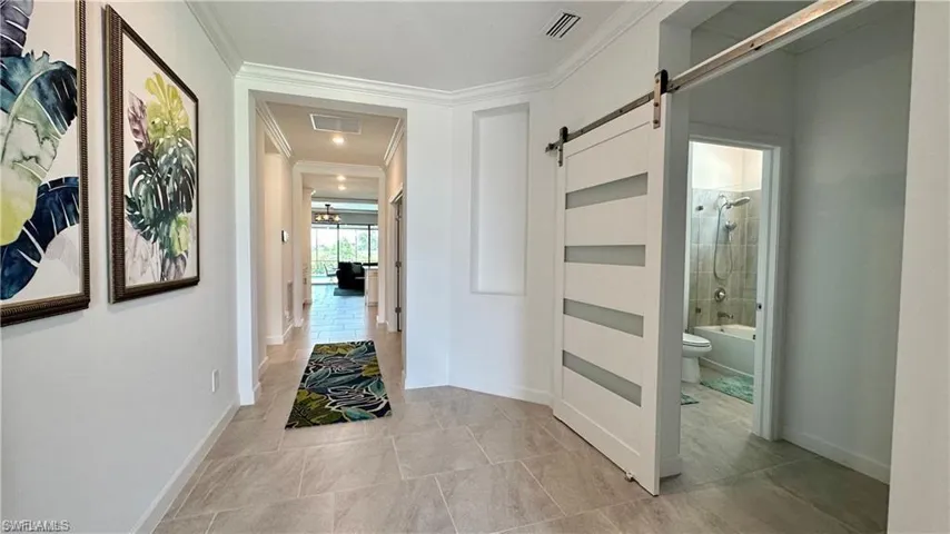 Hall featuring a barn door, crown molding, and light tile flooring