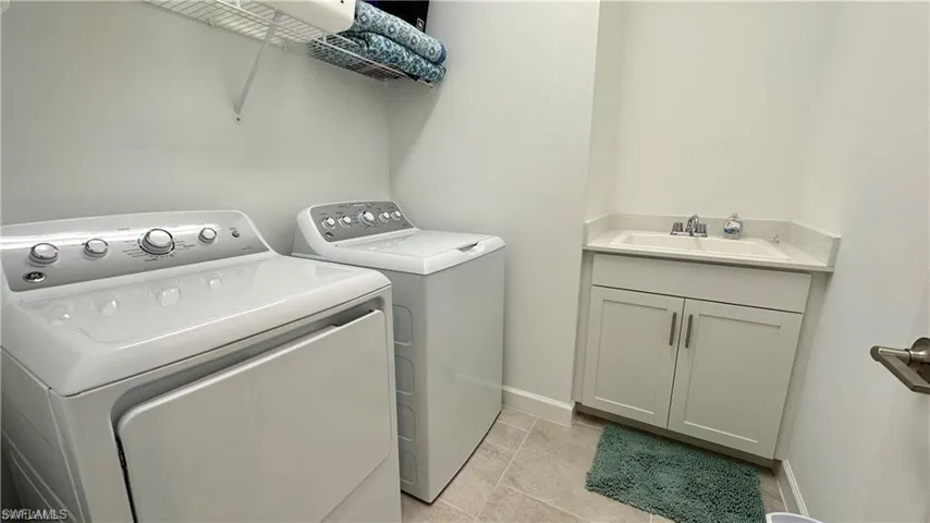 Laundry room featuring sink, independent washer and dryer, light tile floors, and cabinets