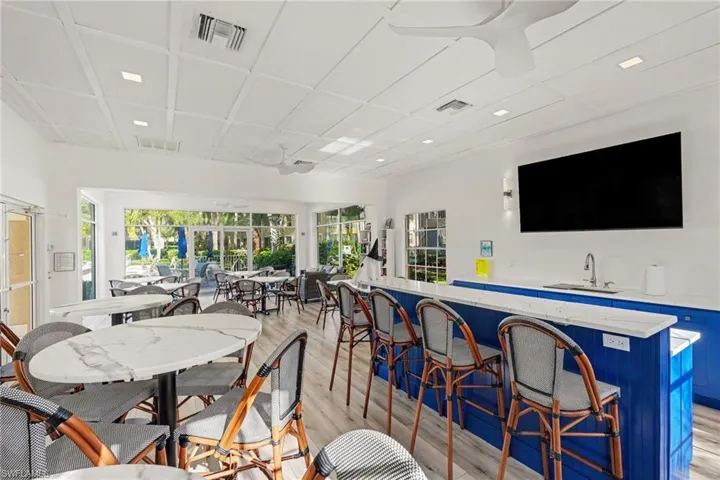 Coffered ceiling with integrated recessed lighting, wood-finish flooring, and a refreshment bar featuring solid-surface countertops, blue cabinetry, and a stainless steel sink