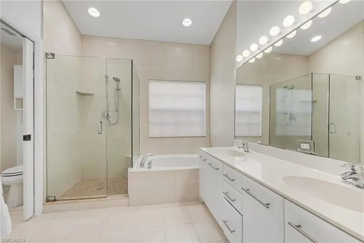 Bathroom featuring a double-sink vanity with light-toned solid surface countertops, a glass-enclosed walk-in shower, a soaking tub, and floor-to-ceiling tile wall finishes