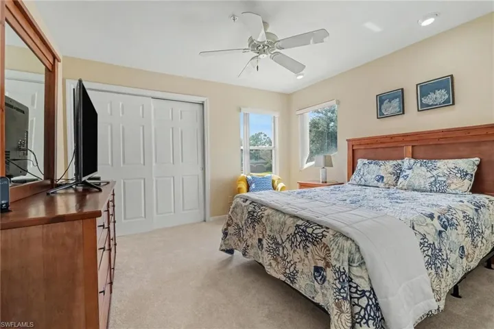 Bedroom featuring neutral wall-to-wall carpeting, two windows with natural light, white sliding closet doors, and a ceiling fan with integrated lighting