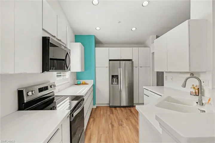 Kitchen featuring flat-panel white cabinetry, solid surface countertops, stainless steel appliances, integrated recessed lighting, and wood-finish flooring