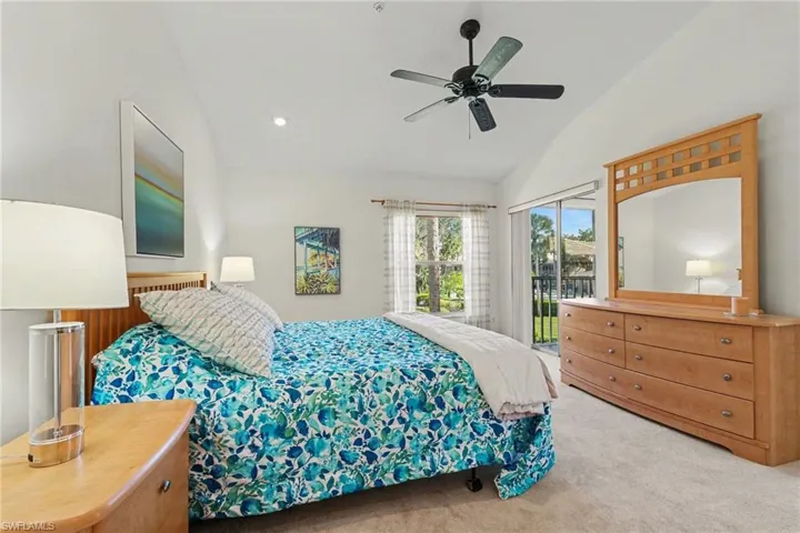 Vaulted ceilings featuring a matte black ceiling fan, neutral carpeting, and a sliding glass door providing external access