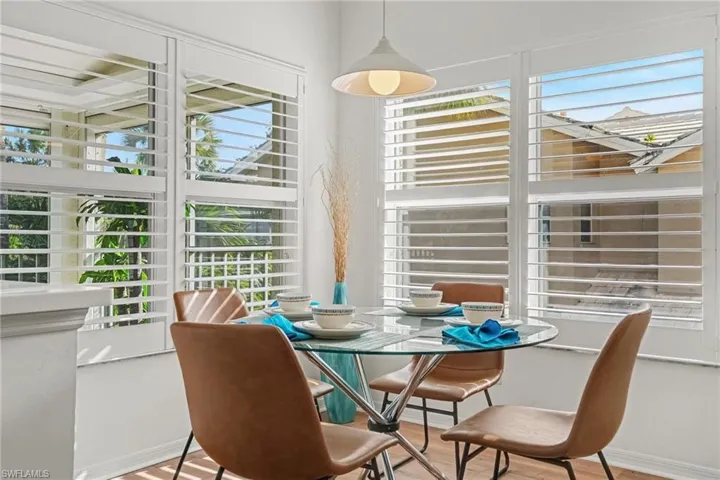Corner dining area featuring large windows with white plantation shutters, neutral walls, and a pendant light fixture
