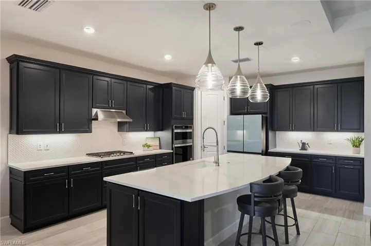 Kitchen with a breakfast bar, sink, hanging light fixtures, a kitchen island with sink, and stainless steel appliances