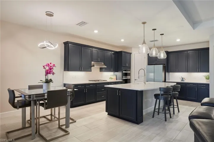 Kitchen with appliances with stainless steel finishes, a kitchen breakfast bar, an island with sink, pendant lighting, and backsplash