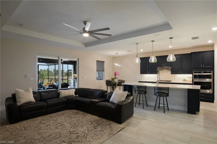 Living room with light hardwood / wood-style floors, ceiling fan, and a tray ceiling