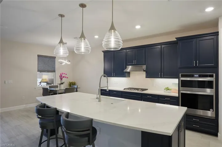 Kitchen with stainless steel appliances, sink, a center island with sink, and decorative light fixtures