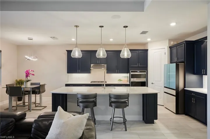 Kitchen featuring fridge, stainless steel double oven, decorative light fixtures, and tasteful backsplash