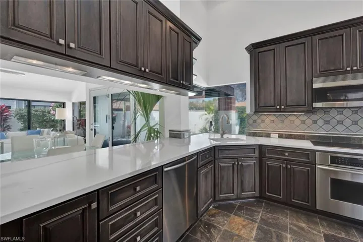 Kitchen featuring stainless steel appliances, decorative backsplash, dark brown cabinets, dark tile patterned flooring, and sink