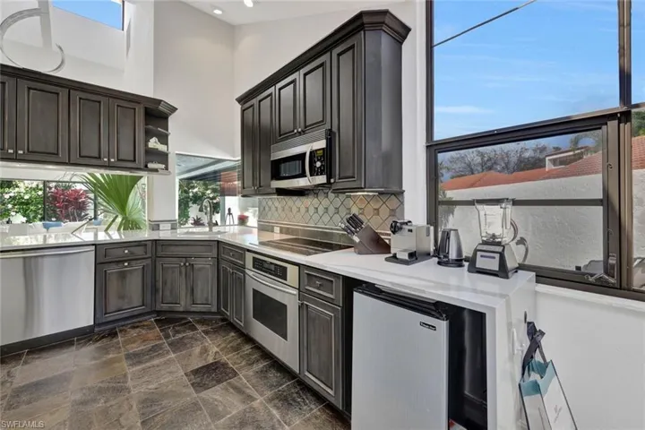 Kitchen with dark tile patterned flooring, stainless steel appliances, decorative backsplash, and plenty of natural light