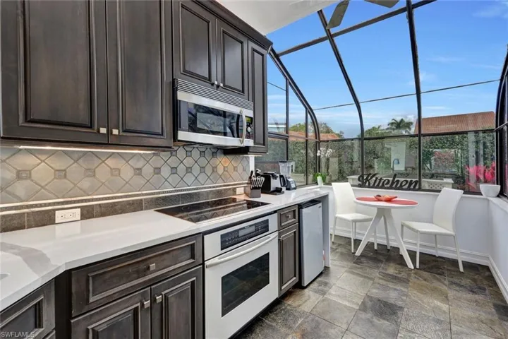 Kitchen featuring dark tile patterned flooring, appliances with stainless steel finishes, decorative backsplash, and dark brown cabinets
