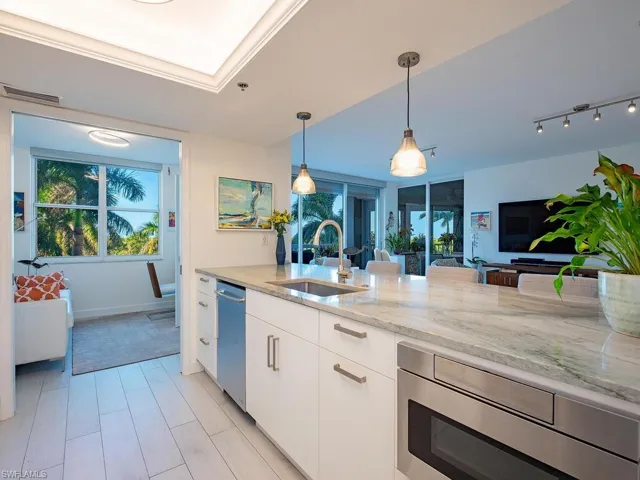 Kitchen with light stone countertops, white cabinets, pendant lighting, stainless steel appliances, and open floor plan