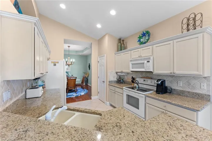 Kitchen with lofted ceiling, light tile patterned floors, an inviting chandelier, white appliances, and a sink