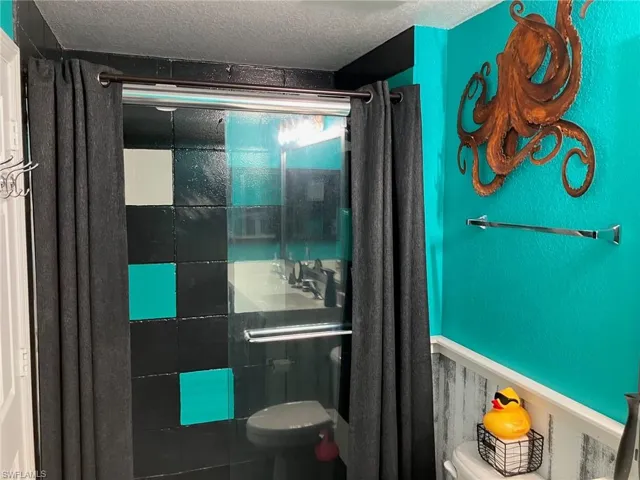 Bathroom with tiled shower, a textured ceiling, and a wainscoted wall