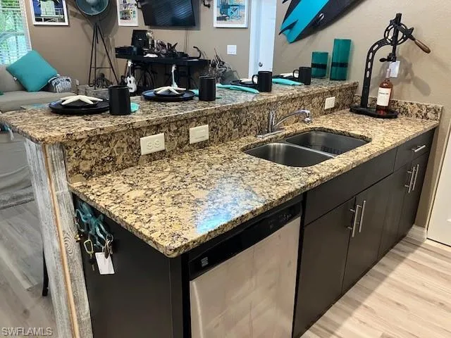 Kitchen with light wood-type flooring, light stone countertops, dark cabinets, and dishwasher