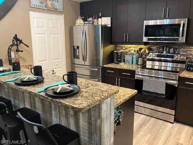 Kitchen featuring a breakfast bar, stainless steel appliances, tasteful backsplash, light stone counters, and light wood-type flooring