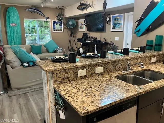 Kitchen featuring light stone countertops, dishwasher, light wood finished floors, open floor plan, and dark cabinets