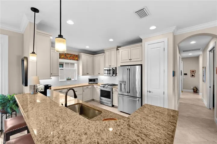 Kitchen featuring light-toned cabinetry, stainless steel appliances, and a spacious island with a built-in sink