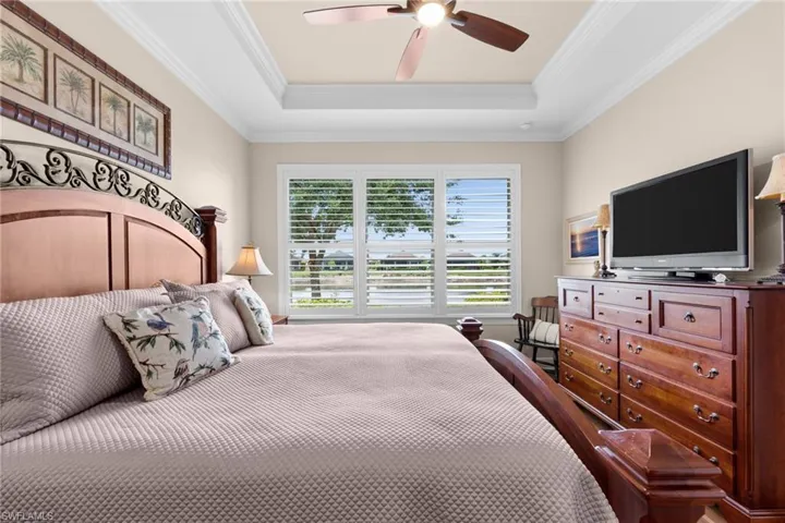 Bedroom featuring a tray ceiling with crown molding, a ceiling fan, and plantation shutters on the window
