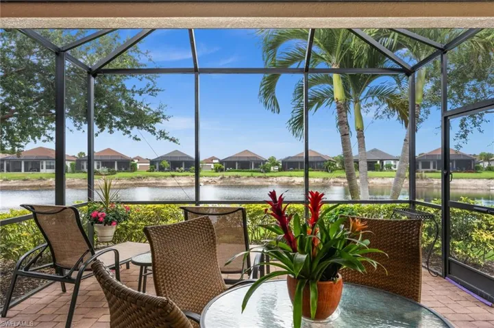 Screened lanai featuring a paver floor, mature landscaping, and a water body backdrop