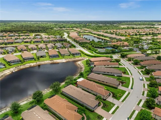 Aerial overview of a residential community featuring multiple homes, a central lake, and lush green landscaping