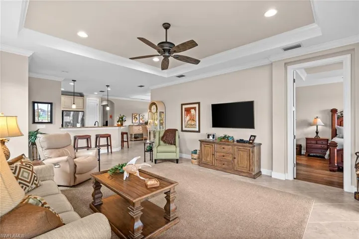 Living area featuring a tray ceiling with crown molding, recessed lighting, and a ceiling fan