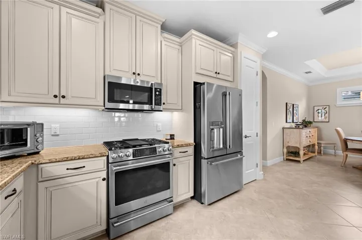 Kitchen featuring stone countertops, white subway tile backsplash, stainless steel appliances, and cream cabinetry with dark hardware