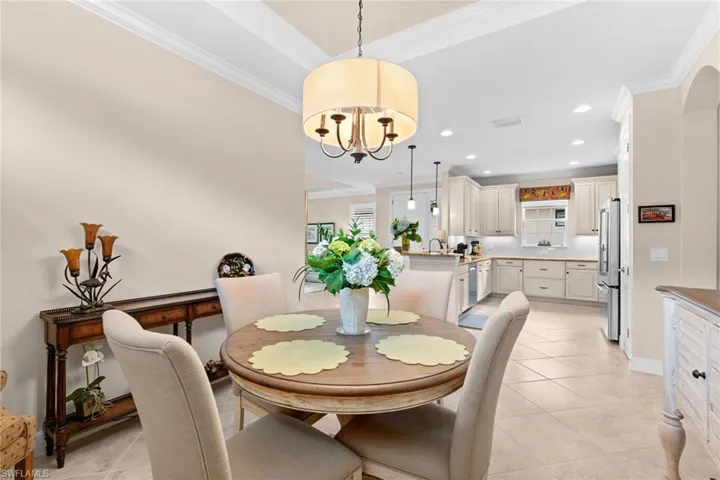 Inviting dining area featuring tray ceilings with crown molding, a drum chandelier, and tiled flooring
